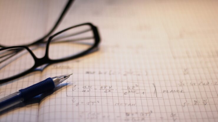 Notebook with physics calculations, pen, and glasses set up for group problem solving