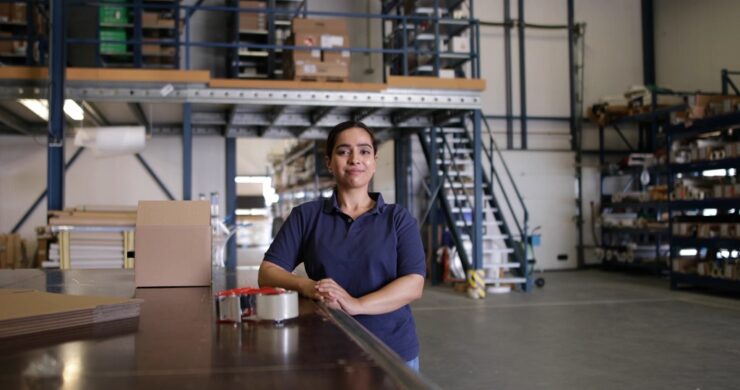 Warehouse worker standing at a packing table with shipping boxes and packing tape in a commercial storage facility