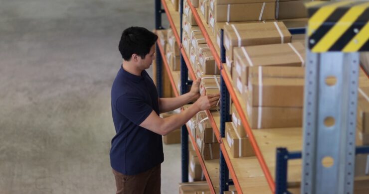 Worker organizing labeled cardboard boxes on warehouse shelving during inventory preparation