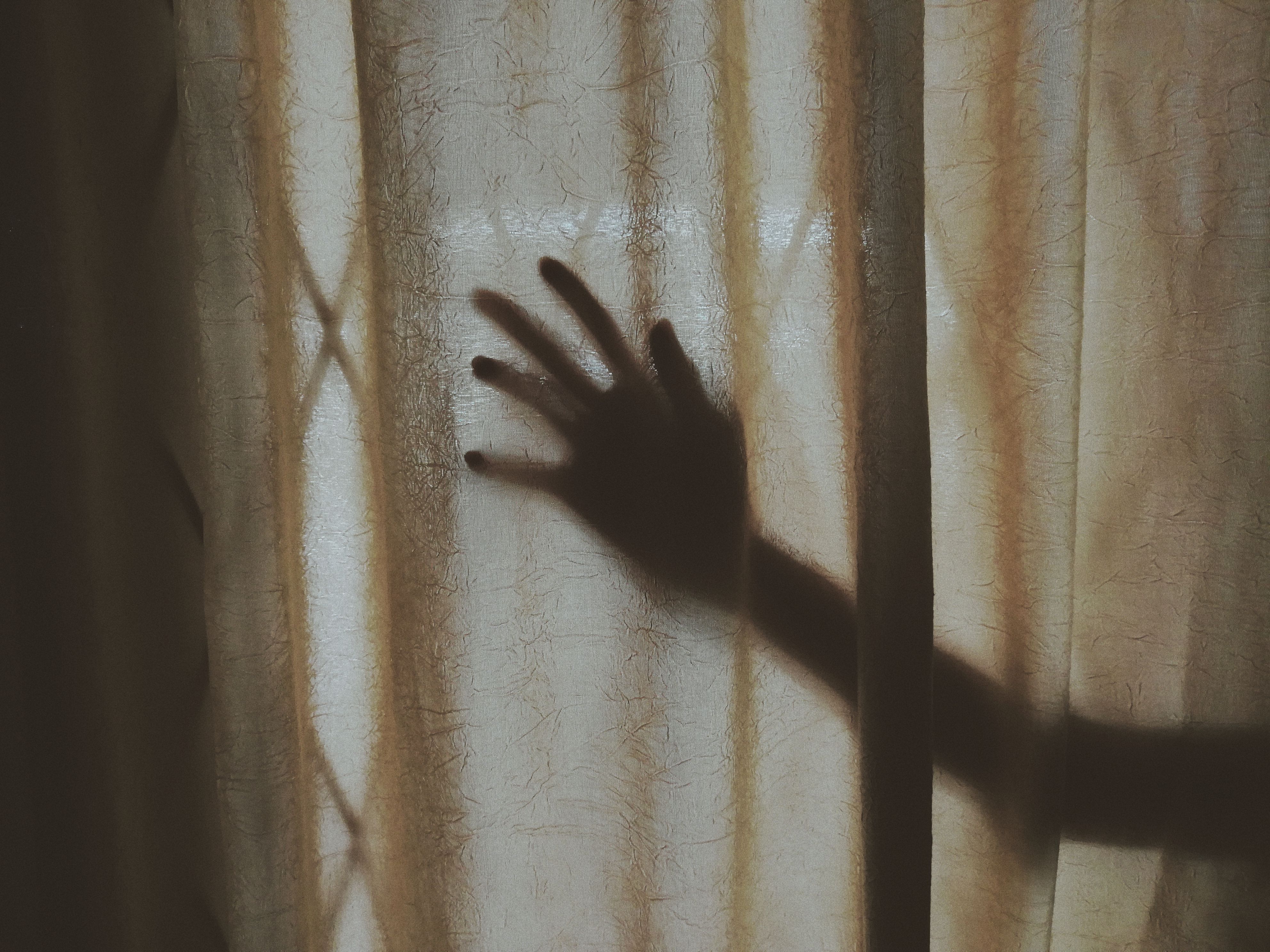 Mysterious hand silhouette casting a shadow on a textured curtain, evoking discretion and privacy